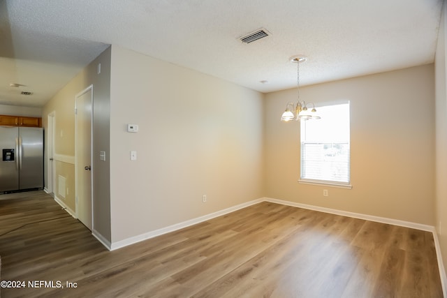 empty room featuring wood-type flooring, a textured ceiling, and a notable chandelier