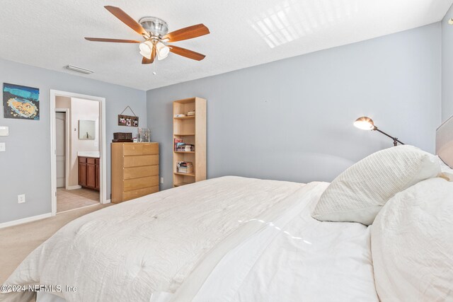 bedroom featuring a spacious closet, ensuite bath, a textured ceiling, light colored carpet, and ceiling fan