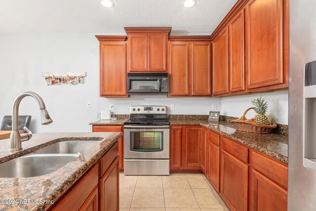 kitchen featuring stainless steel electric range, light tile patterned flooring, dark stone counters, a textured ceiling, and sink