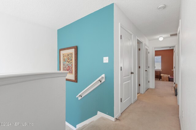 hallway with a textured ceiling and light carpet