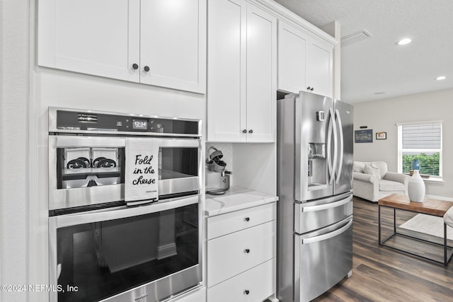 kitchen with dark wood-type flooring, a textured ceiling, light stone countertops, white cabinetry, and appliances with stainless steel finishes