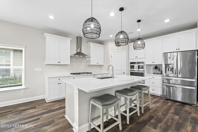 kitchen featuring wall chimney exhaust hood, sink, an island with sink, white cabinetry, and appliances with stainless steel finishes