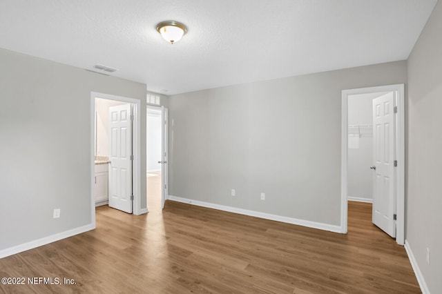 unfurnished bedroom with a closet, a walk in closet, wood-type flooring, a textured ceiling, and ensuite bathroom