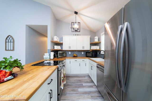 kitchen with stainless steel appliances, white cabinetry, wood counters, pendant lighting, and lofted ceiling