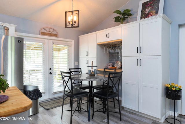 dining area featuring french doors, light hardwood / wood-style flooring, vaulted ceiling, and an inviting chandelier