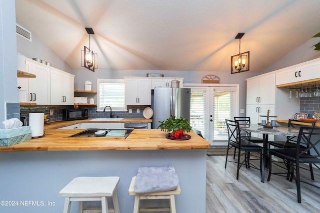 kitchen featuring white cabinets, kitchen peninsula, black appliances, hanging light fixtures, and butcher block countertops