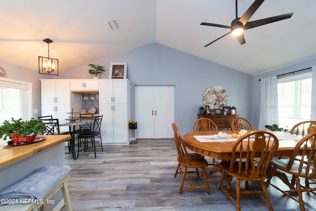 dining space featuring light hardwood / wood-style floors, ceiling fan with notable chandelier, lofted ceiling, and a wealth of natural light