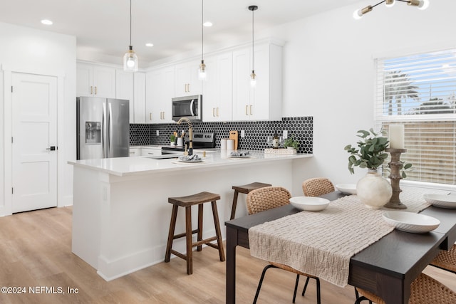 kitchen featuring white cabinetry, appliances with stainless steel finishes, hanging light fixtures, kitchen peninsula, and light hardwood / wood-style flooring