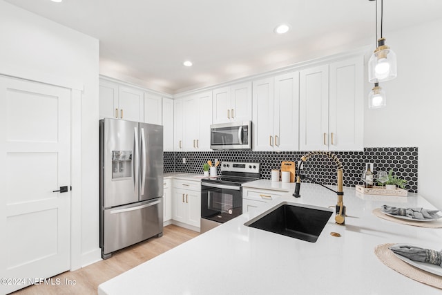 kitchen featuring appliances with stainless steel finishes, light wood-type flooring, white cabinets, pendant lighting, and decorative backsplash