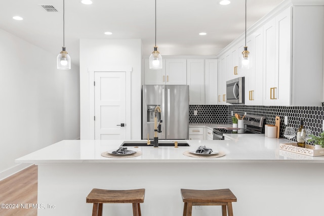 kitchen featuring white cabinets, kitchen peninsula, a kitchen breakfast bar, pendant lighting, and appliances with stainless steel finishes