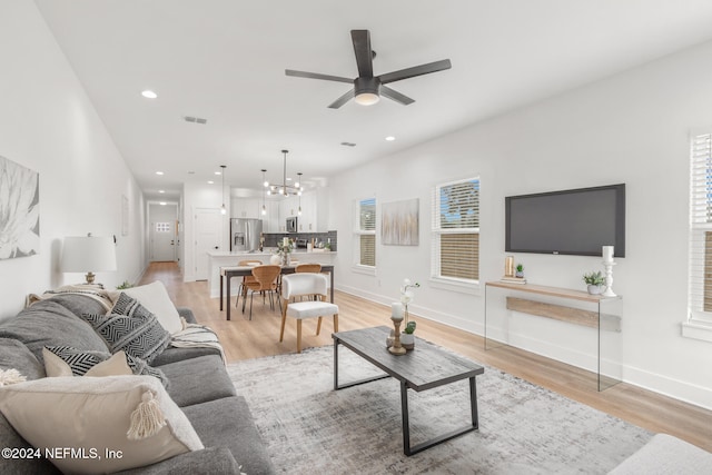 living room featuring ceiling fan with notable chandelier and light hardwood / wood-style floors