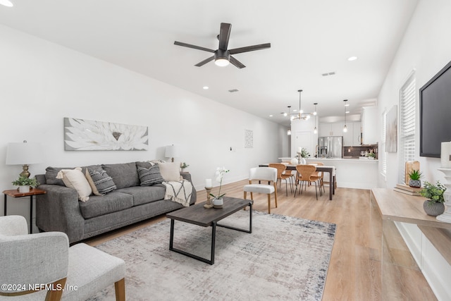 living room with light hardwood / wood-style floors and ceiling fan with notable chandelier