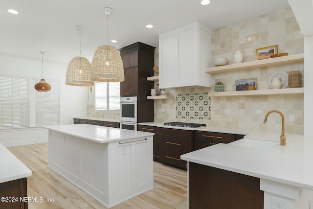 kitchen featuring light wood-type flooring, dark brown cabinetry, stainless steel gas cooktop, sink, and decorative light fixtures