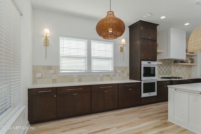 kitchen featuring decorative backsplash, white double oven, gas stovetop, light hardwood / wood-style floors, and hanging light fixtures