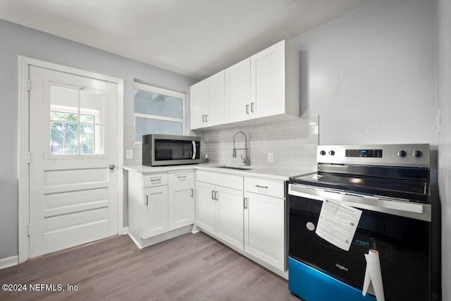 kitchen featuring light hardwood / wood-style floors, white cabinetry, sink, appliances with stainless steel finishes, and tasteful backsplash