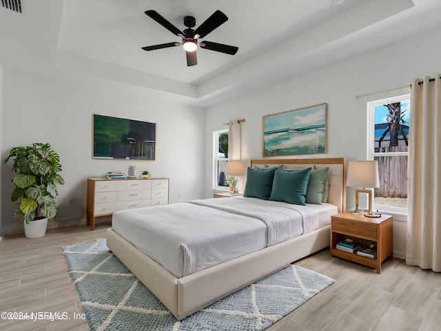 bedroom with multiple windows, ceiling fan, and a raised ceiling