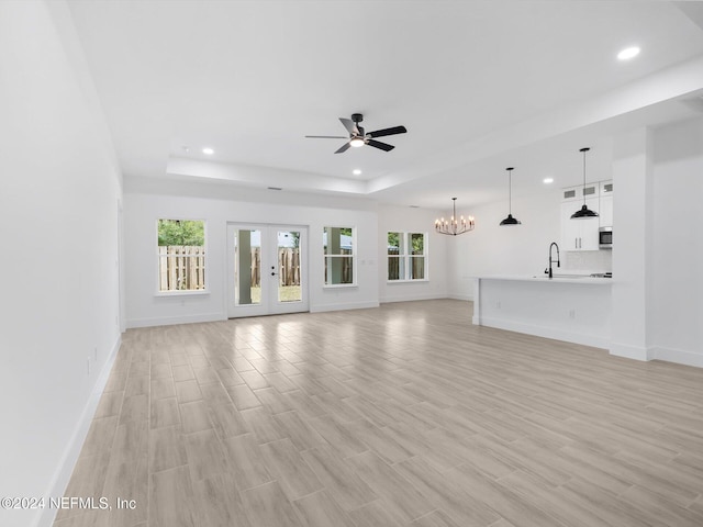 unfurnished living room with light wood-type flooring, ceiling fan with notable chandelier, and a tray ceiling