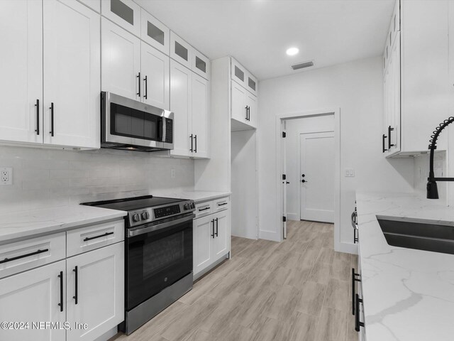 kitchen featuring light stone counters, white cabinetry, range with electric cooktop, sink, and light hardwood / wood-style floors