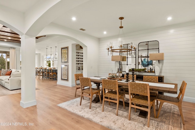 dining space with wood walls, an inviting chandelier, and light hardwood / wood-style flooring