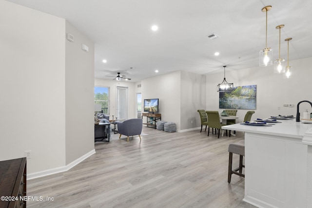 interior space with ceiling fan with notable chandelier, hanging light fixtures, sink, a kitchen breakfast bar, and light hardwood / wood-style flooring