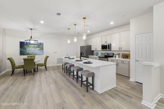 kitchen with white cabinetry, stainless steel appliances, hanging light fixtures, and a center island with sink