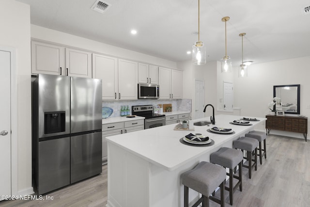 kitchen with light wood-type flooring, appliances with stainless steel finishes, decorative backsplash, and a center island with sink