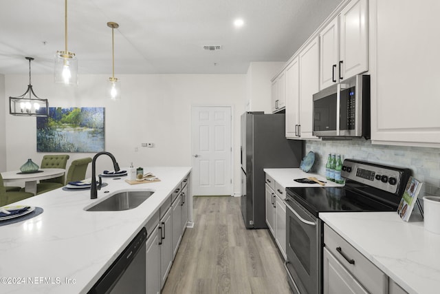 kitchen featuring appliances with stainless steel finishes, hanging light fixtures, sink, light hardwood / wood-style floors, and white cabinets