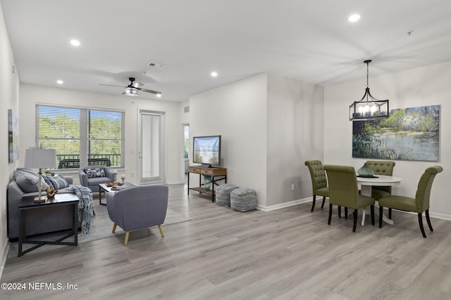 living room with ceiling fan with notable chandelier and light hardwood / wood-style floors