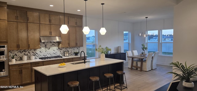 kitchen with tasteful backsplash, light countertops, under cabinet range hood, stainless steel gas cooktop, and a sink