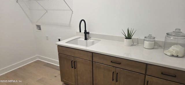 clothes washing area with light wood finished floors, baseboards, a sink, hookup for a washing machine, and electric dryer hookup