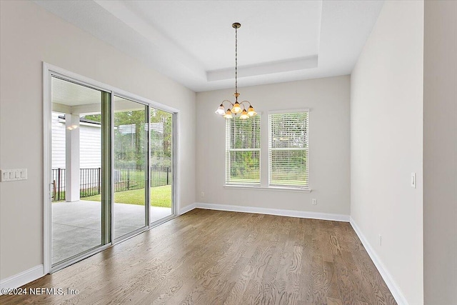 spare room with hardwood / wood-style floors, a chandelier, and a raised ceiling