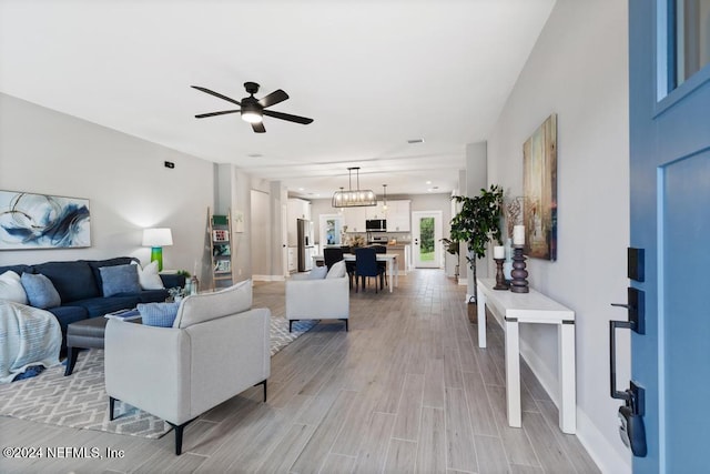 living room featuring light wood-type flooring and ceiling fan with notable chandelier