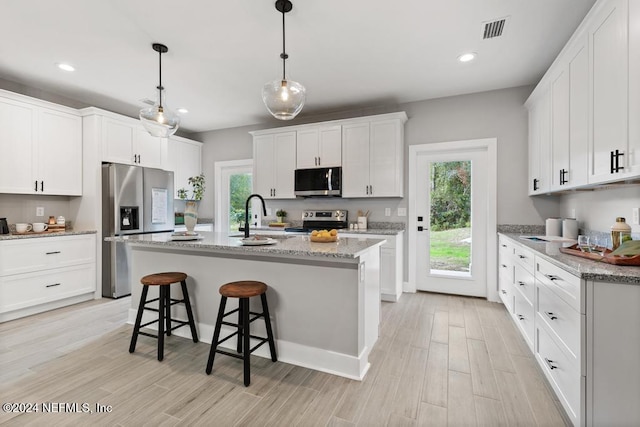 kitchen featuring a center island with sink, white cabinetry, appliances with stainless steel finishes, pendant lighting, and light hardwood / wood-style flooring