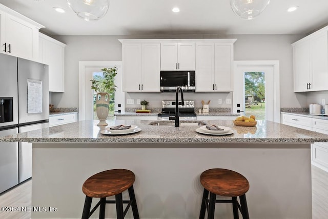 kitchen featuring stainless steel appliances, white cabinets, an island with sink, and sink