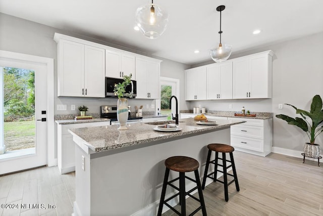 kitchen featuring white cabinetry, stainless steel appliances, decorative light fixtures, and an island with sink