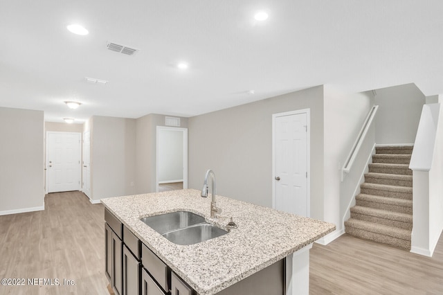 kitchen featuring light hardwood / wood-style floors, sink, light stone counters, and an island with sink