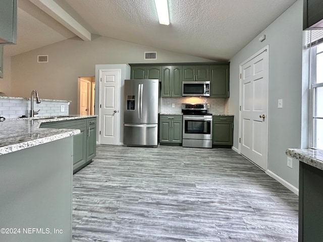 kitchen featuring lofted ceiling with beams, appliances with stainless steel finishes, green cabinetry, sink, and decorative backsplash