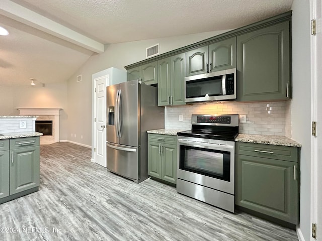 kitchen with decorative backsplash, appliances with stainless steel finishes, vaulted ceiling with beams, and light hardwood / wood-style flooring