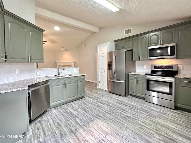 kitchen featuring lofted ceiling with beams, tasteful backsplash, stainless steel appliances, light wood-type flooring, and sink