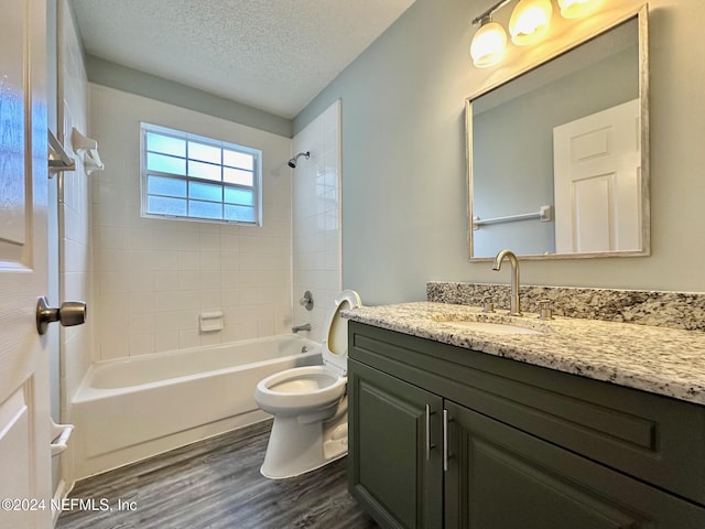 full bathroom featuring wood-type flooring, vanity, a textured ceiling, toilet, and tiled shower / bath