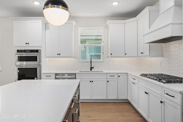 kitchen with white cabinets, light hardwood / wood-style floors, custom range hood, and appliances with stainless steel finishes