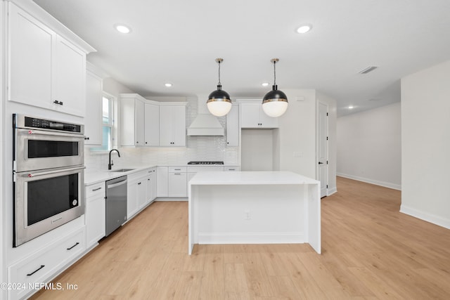 kitchen with premium range hood, stainless steel appliances, white cabinetry, light hardwood / wood-style flooring, and a kitchen island