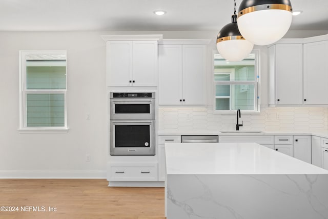 kitchen featuring stainless steel appliances, sink, pendant lighting, light hardwood / wood-style floors, and white cabinetry