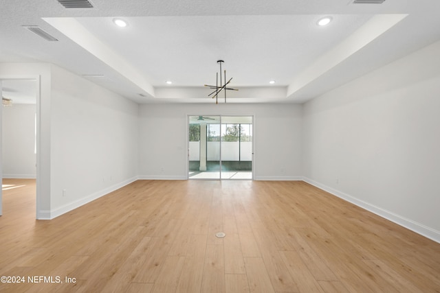 unfurnished room featuring a raised ceiling, a chandelier, and light hardwood / wood-style floors