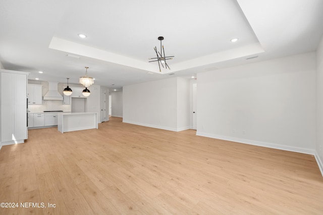 unfurnished living room featuring a tray ceiling, light hardwood / wood-style flooring, and a notable chandelier