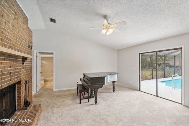 interior space with a brick fireplace, a textured ceiling, light colored carpet, ceiling fan, and lofted ceiling