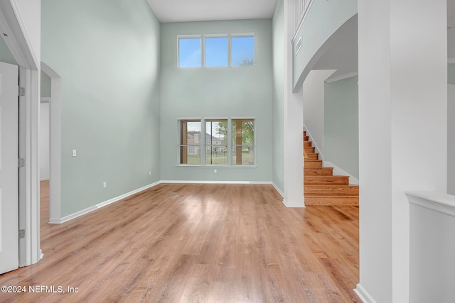 unfurnished living room with light wood-type flooring, a wealth of natural light, and a high ceiling