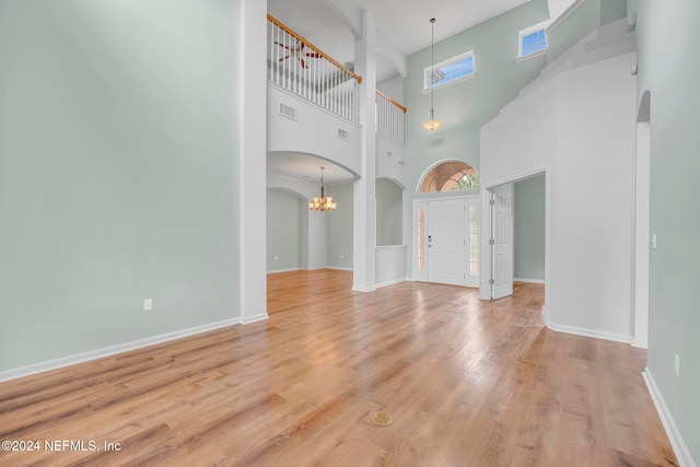 unfurnished living room with a high ceiling, light wood-type flooring, and a chandelier