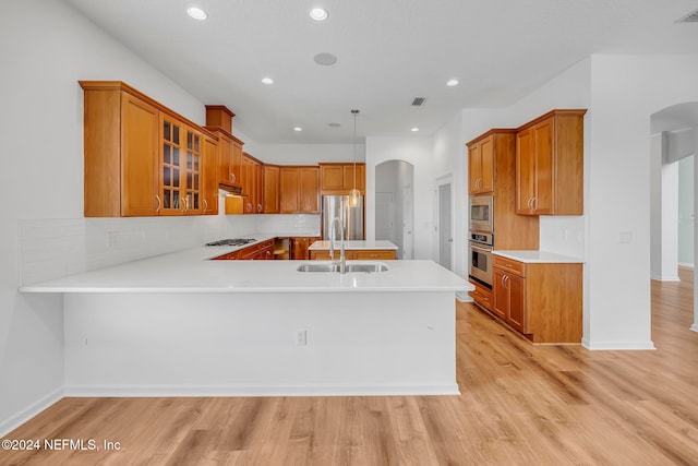 kitchen with kitchen peninsula, appliances with stainless steel finishes, sink, and light hardwood / wood-style flooring