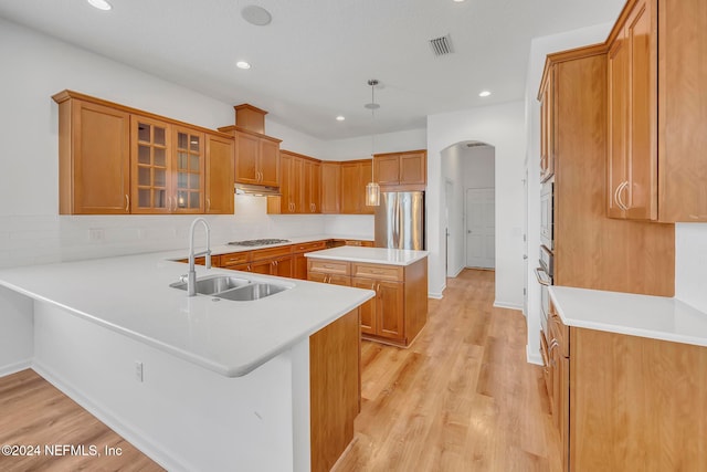 kitchen featuring stainless steel appliances, decorative light fixtures, sink, kitchen peninsula, and light hardwood / wood-style flooring